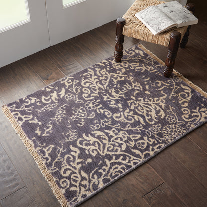 Purple & cream arabesque patterned rug with fringed ends on a dark wood floor.