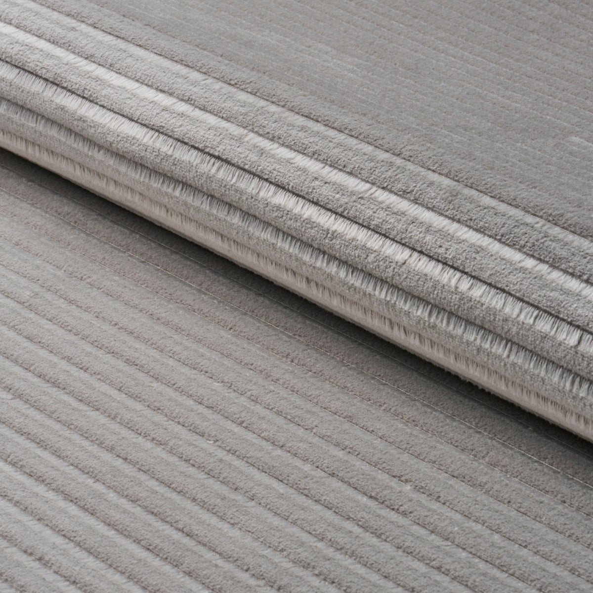 Grey ribbed rug, rolled up, showing soft plush pile and textured stripes.