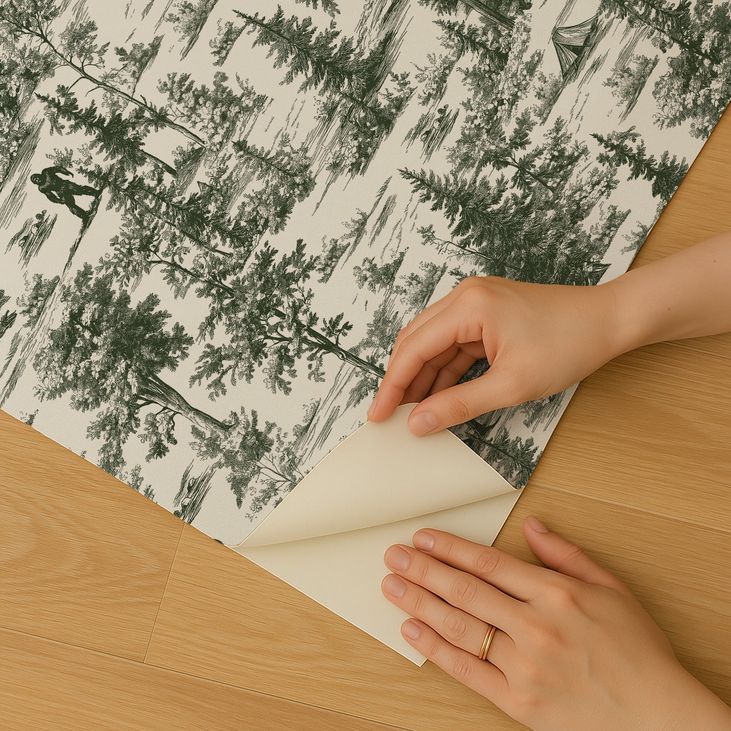 Hands peel back a forest-patterned sheet of paper on a wooden table; grayscale green trees on cream background.