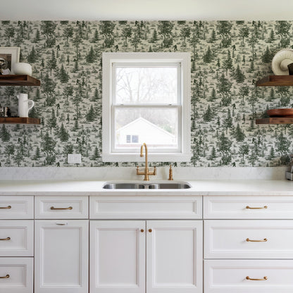 White kitchen with forest wallpaper, brass faucet, double sink, white cabinetry, and open wooden shelves.