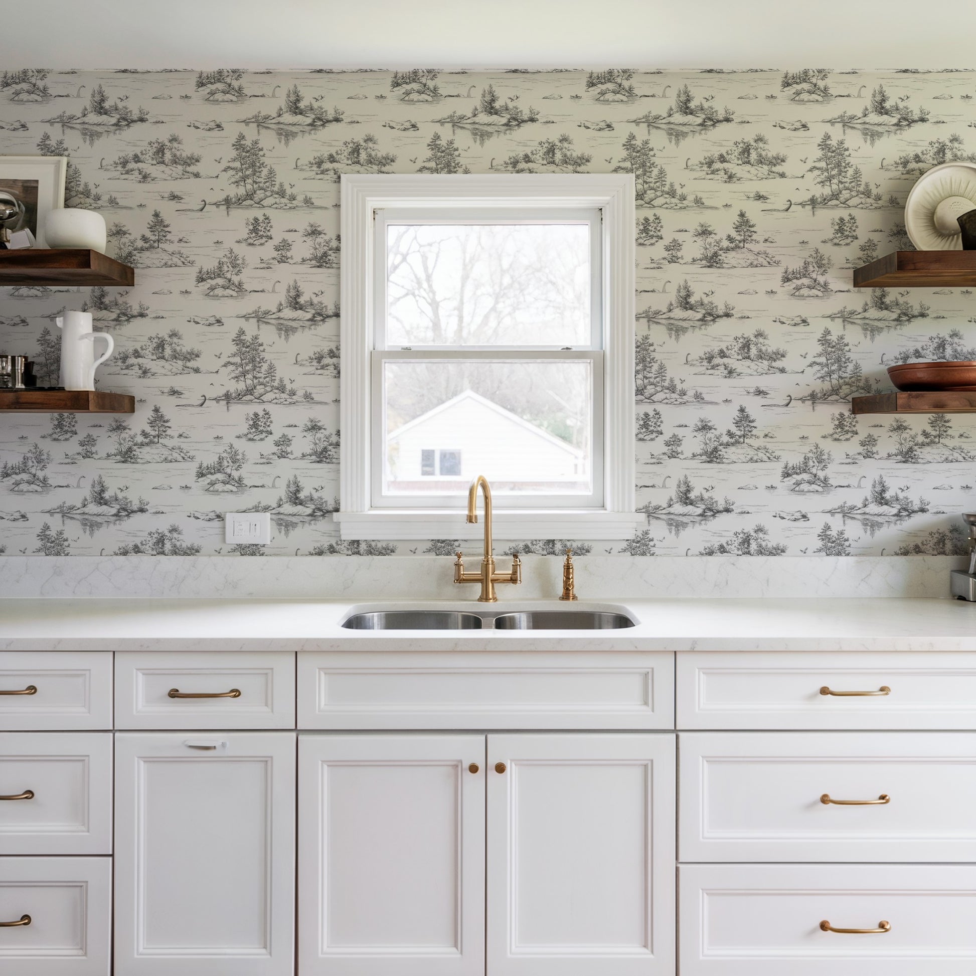 Bright white shaker kitchen with brass faucet and hardware, double-basin sink under a window, toile wallpaper and open wooden shelves.