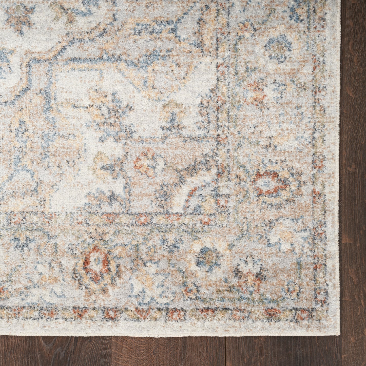 Distressed ivory oriental rug with blue, beige and rust motifs and a decorative border on a dark hardwood floor.
