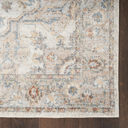 Distressed ivory oriental rug with blue, beige and rust motifs and a decorative border on a dark hardwood floor.