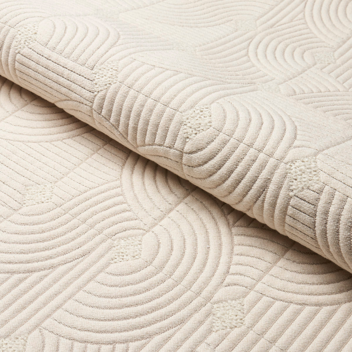 Cream quilted blanket with concentric circular stitching, plush texture and folded edge.