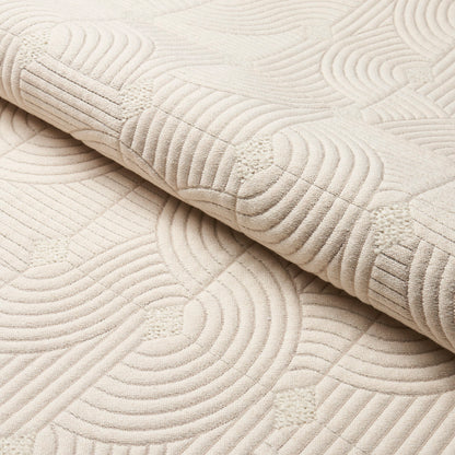 Cream quilted blanket with concentric circular stitching, plush texture and folded edge.