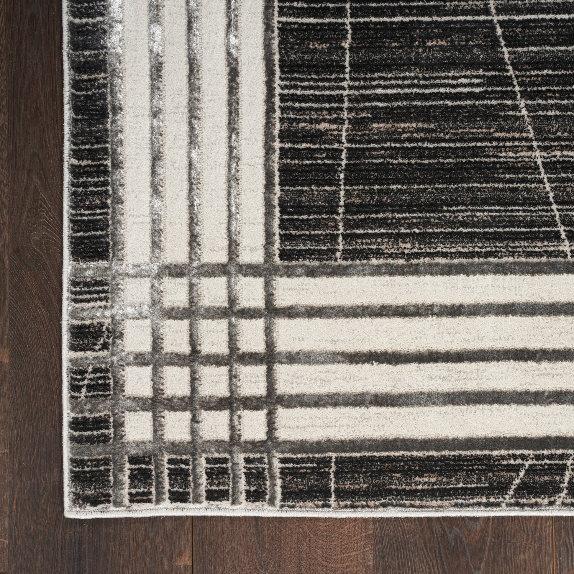 Flat-weave geometric area rug in black, gray, and cream with grid border on dark hardwood floor.