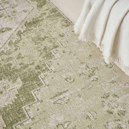 Olive green and beige distressed oriental rug with geometric border; woven texture, cream fringe throw draped at edge.