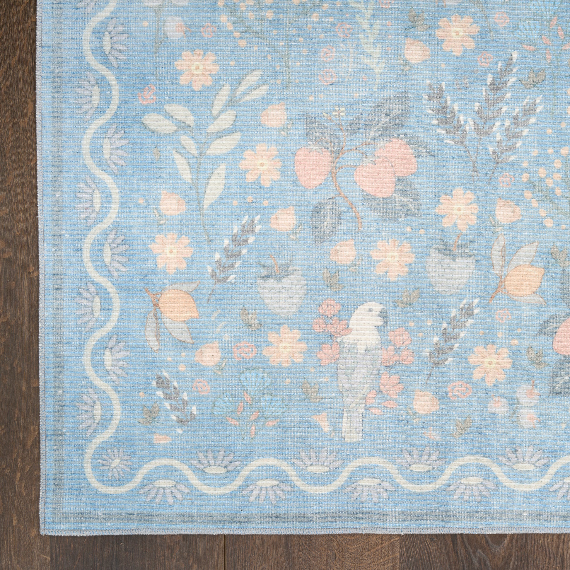 Blue woven area rug with pale pink flowers and white scalloped border on a wooden floor.
