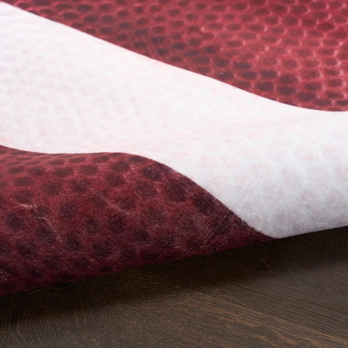 Close-up of a burgundy pebble-textured felt throw with pale pink underside on wood.