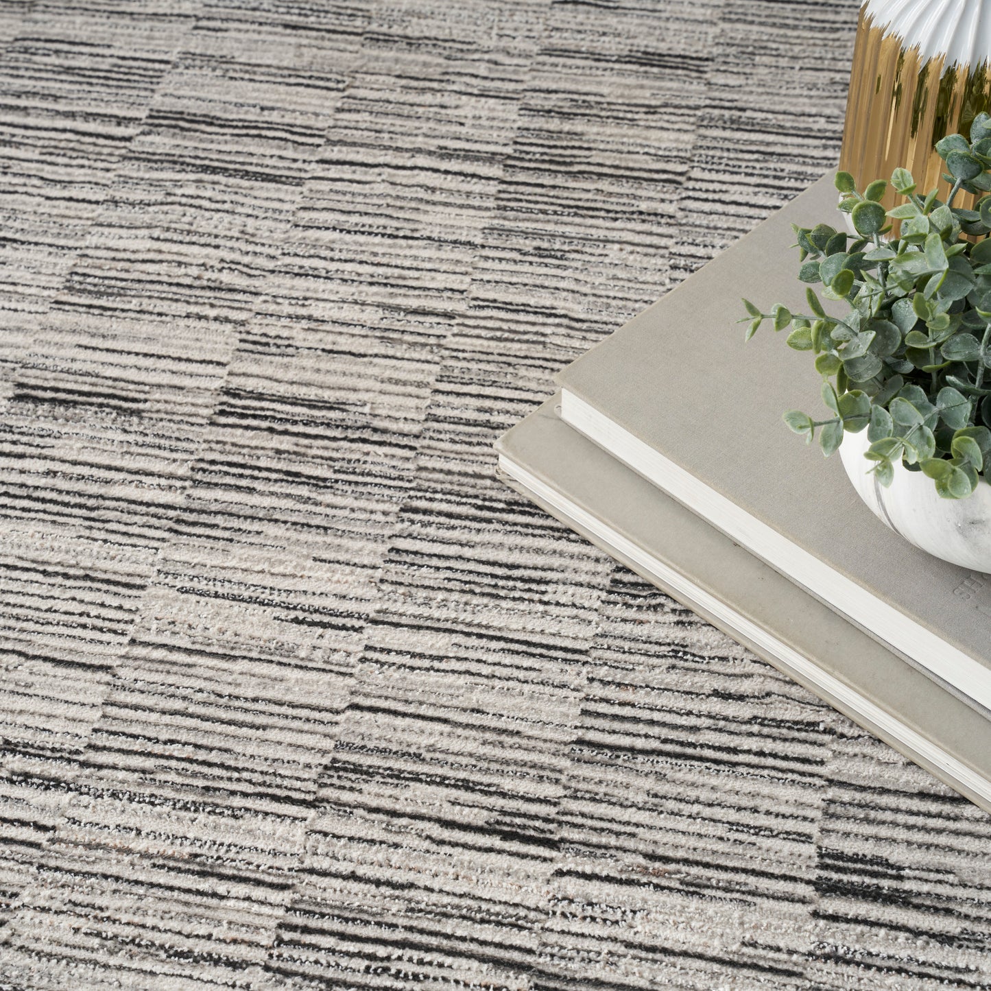 Beige-gray geometric rug with stacked neutral books, a small potted succulent, and a gold vase in a chic home decor scene.