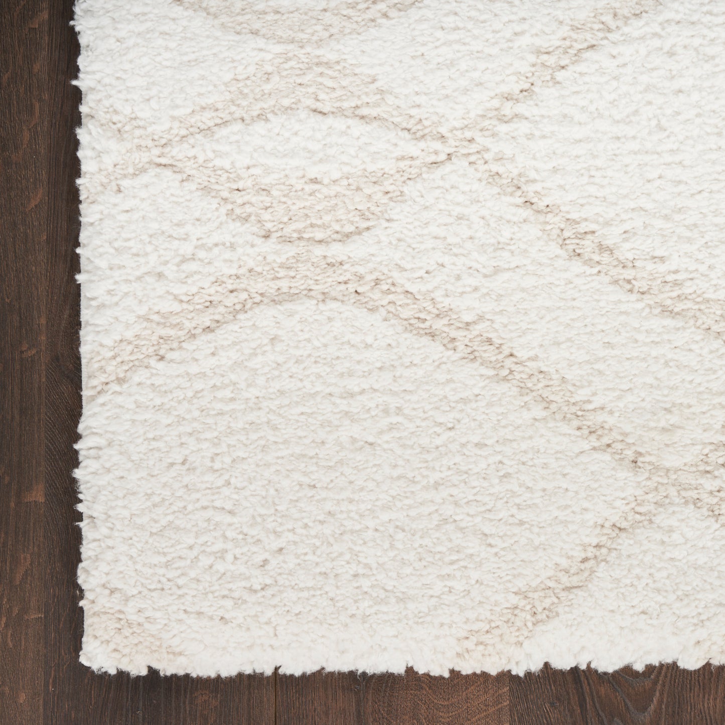 Cream shag rug with plush pile and subtle circular swirl pattern on dark wood floor.