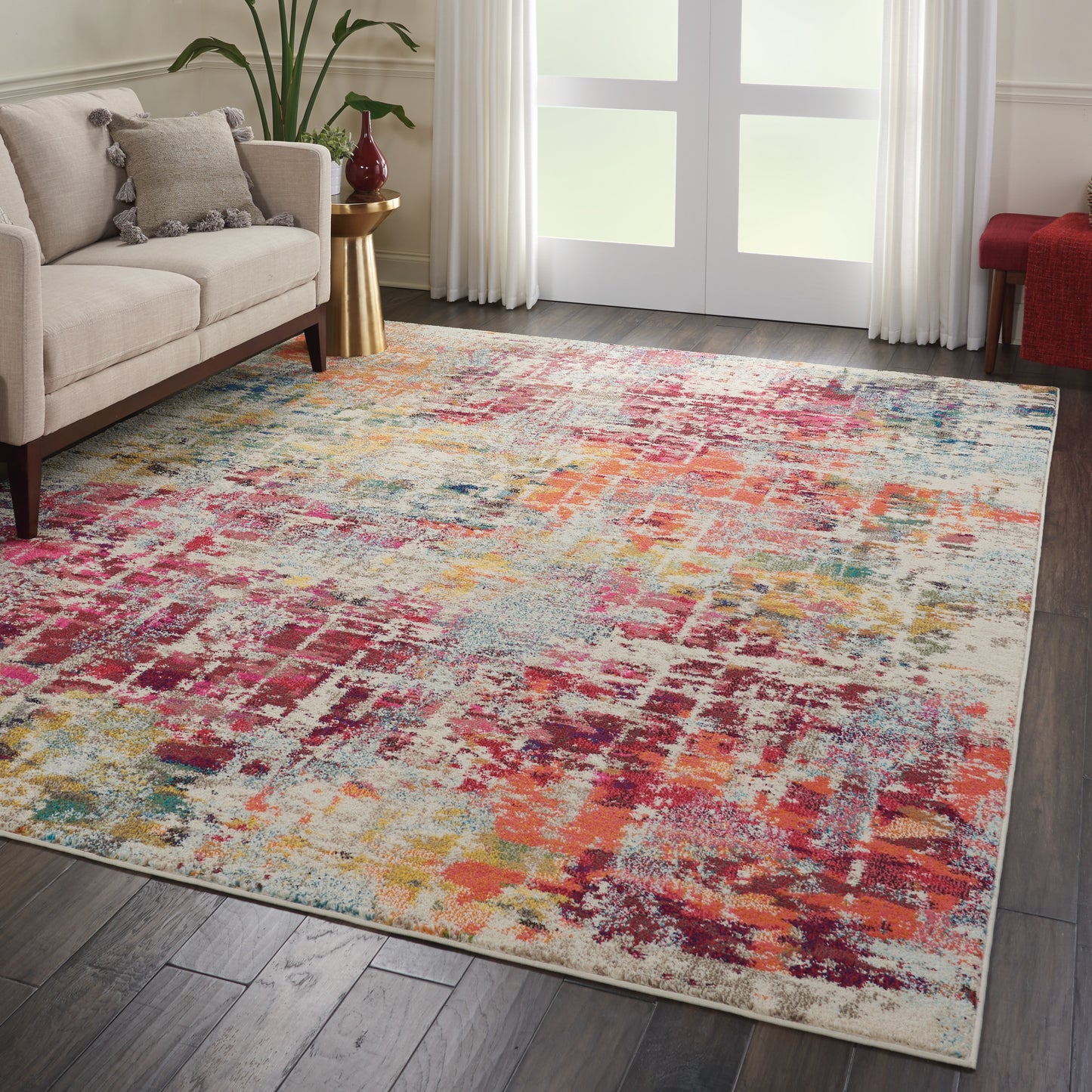 Abstract multicolor area rug in pink, orange, teal and beige tones on a dark wood floor beside a cream sofa.