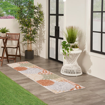 Indoor patio runner rug with orange floral mandalas and pale blue accents on dark wood floor beside white wicker plant stand and black-framed doors.