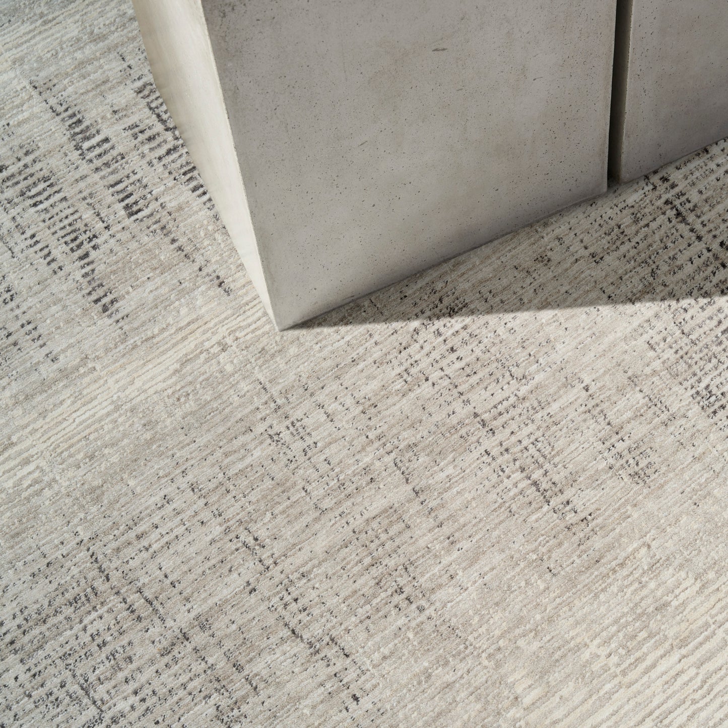 Light gray concrete block corner resting on a textured beige rug with subtle linear patterns.