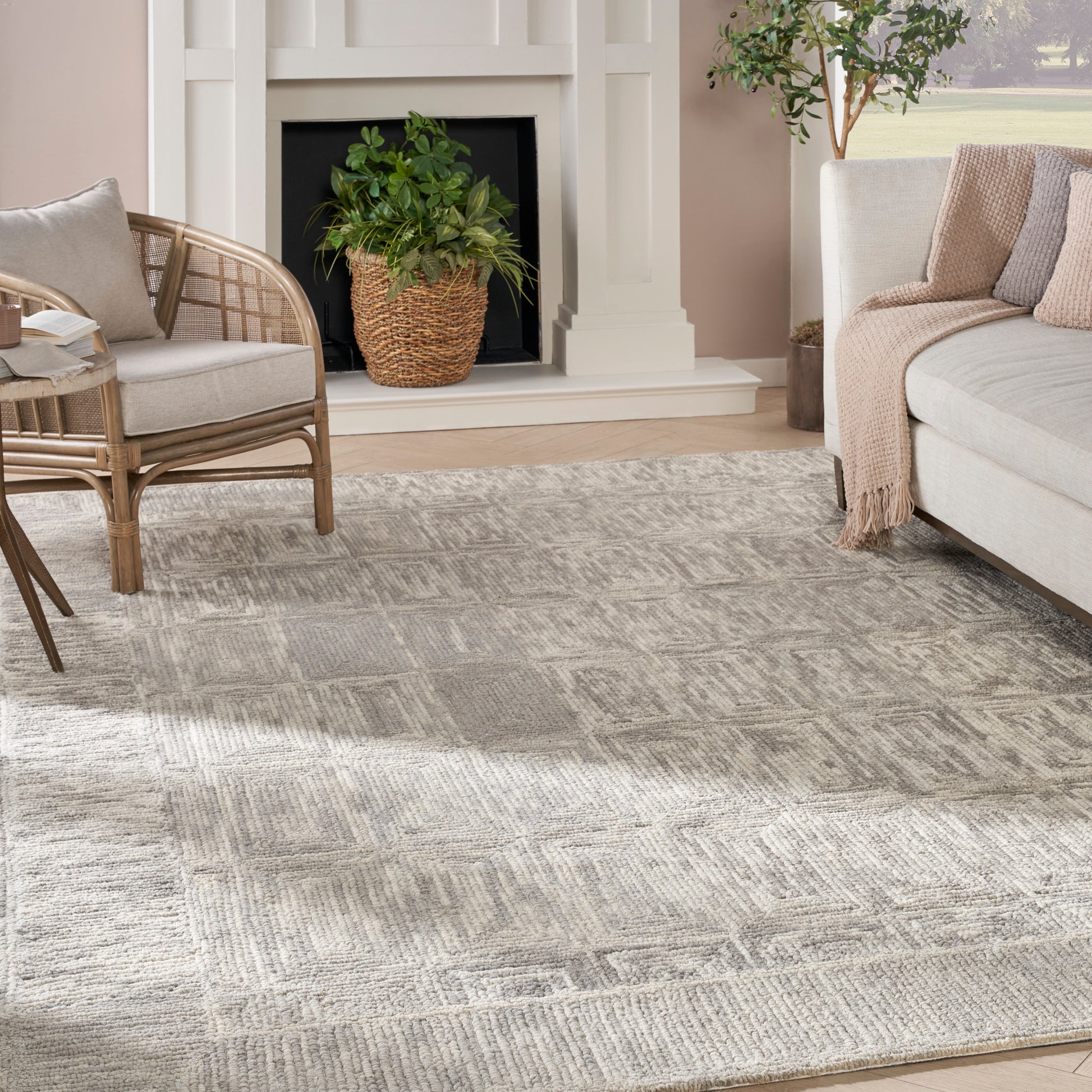 Cozy living room with a beige-gray geometric rug, wicker chair, light sofa with throw, and potted plant by a white fireplace