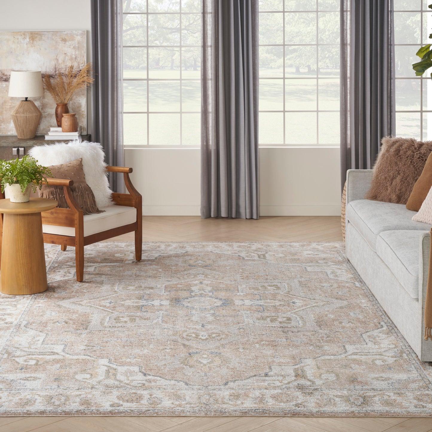 Neutral living room with beige-gray oriental rug, light gray sofa, wooden armchair, round side table, plant, gray curtains.