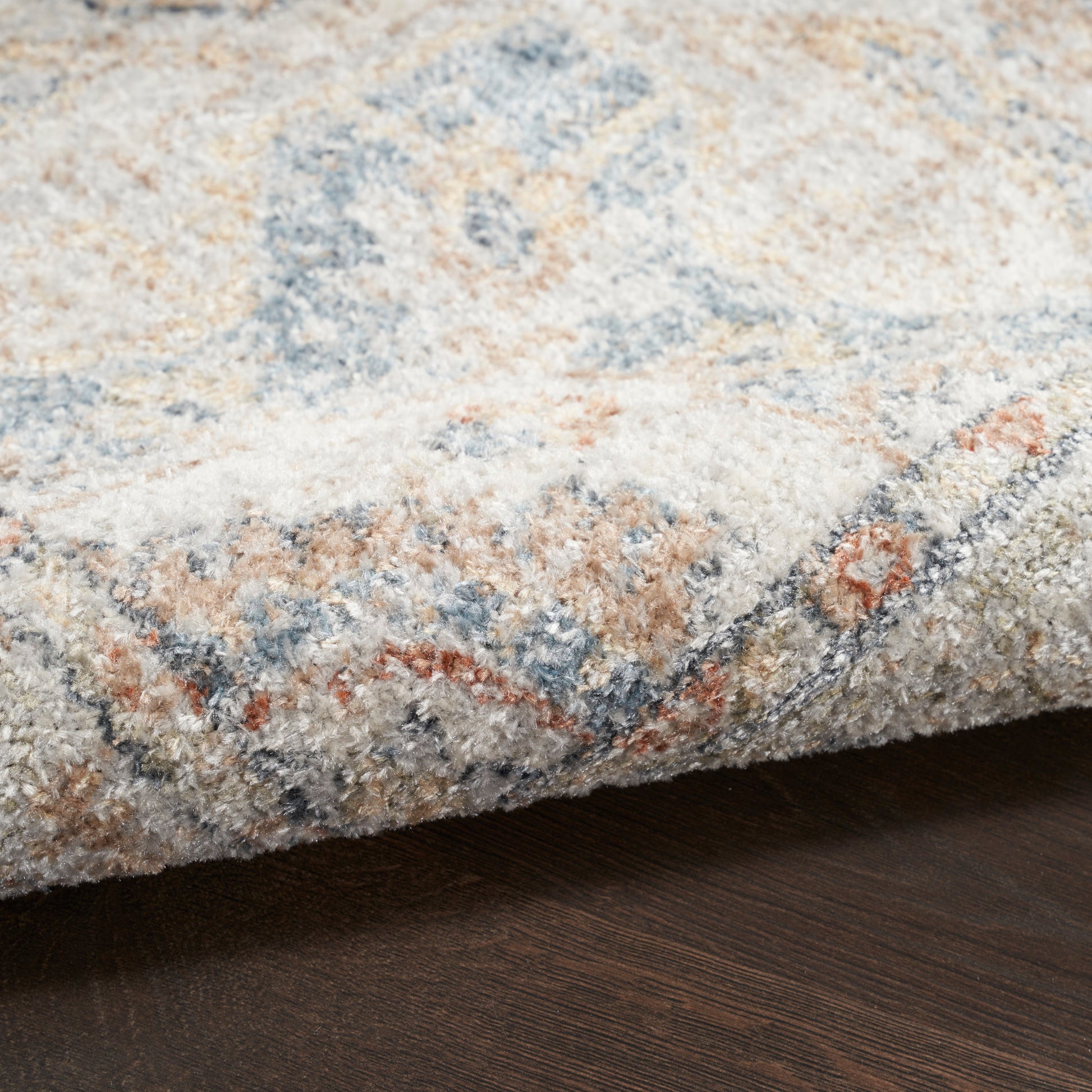 Soft textured area rug with cream, blue, beige and rust geometric pattern; folded edge on dark wood floor.
