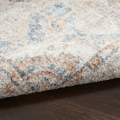 Soft textured area rug with cream, blue, beige and rust geometric pattern; folded edge on dark wood floor.