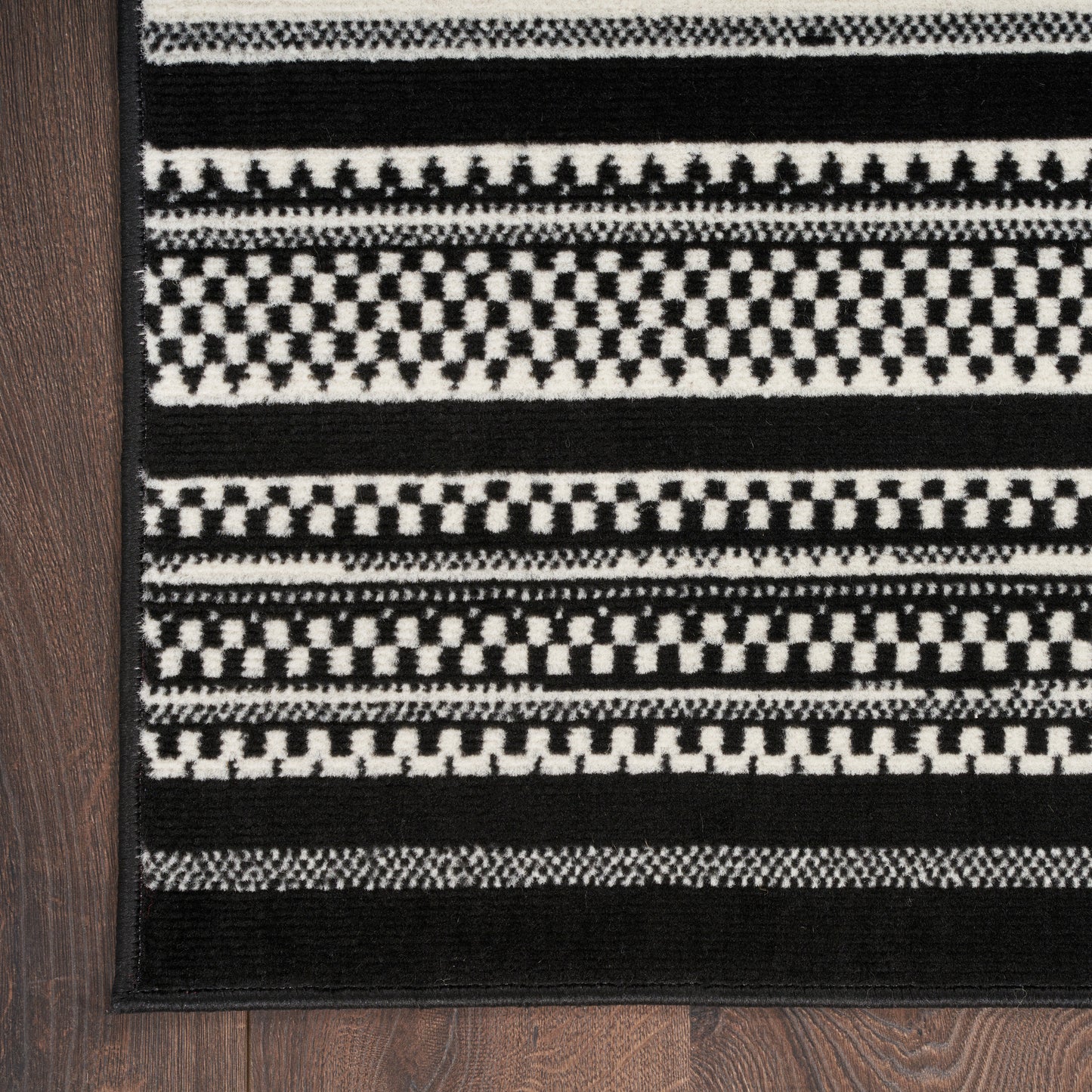 Black and white woven runner rug with geometric stripes and checkerboard bands on a dark wood floor.