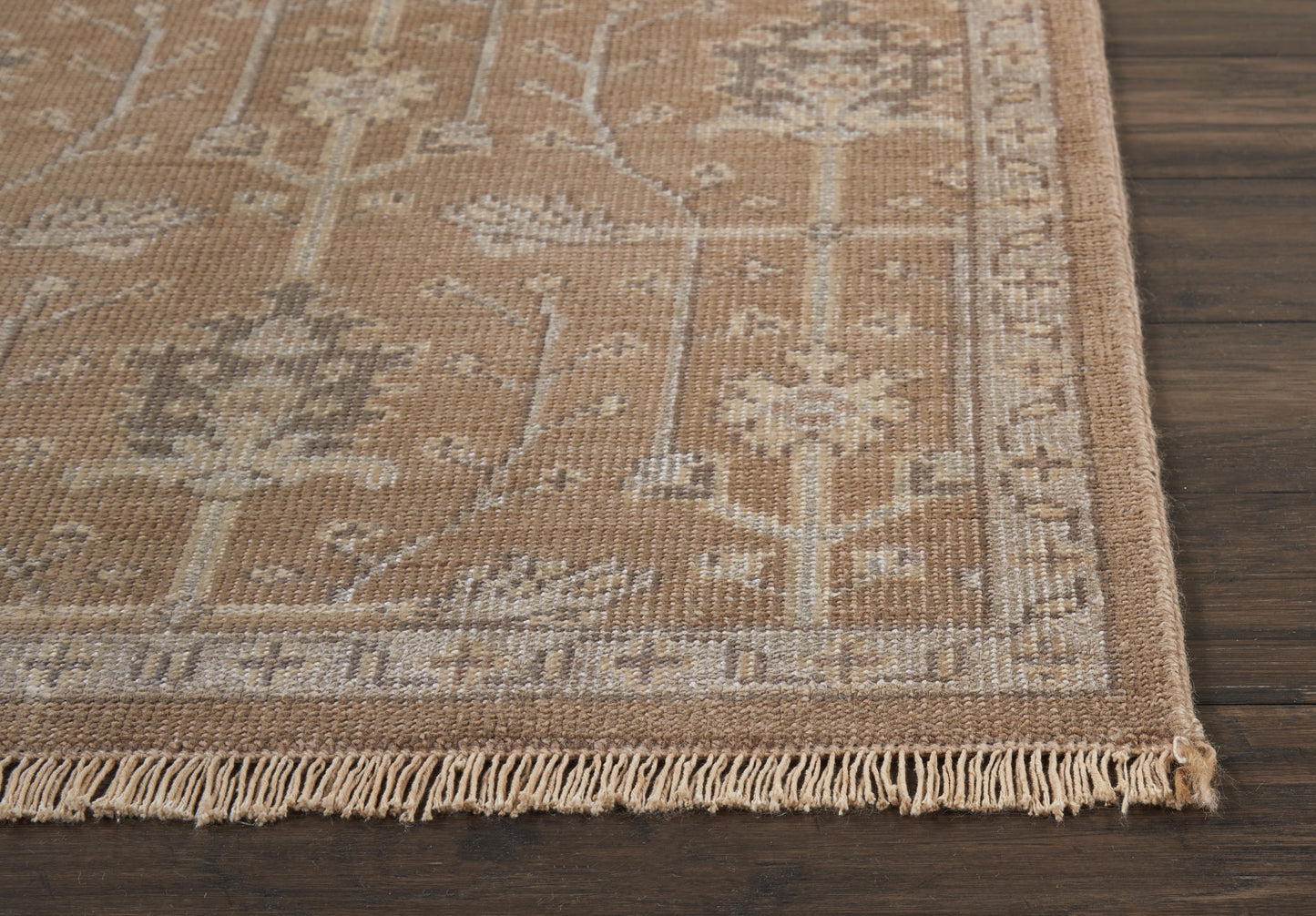 Beige oriental rug with floral border and tassel fringe on dark wood floor.