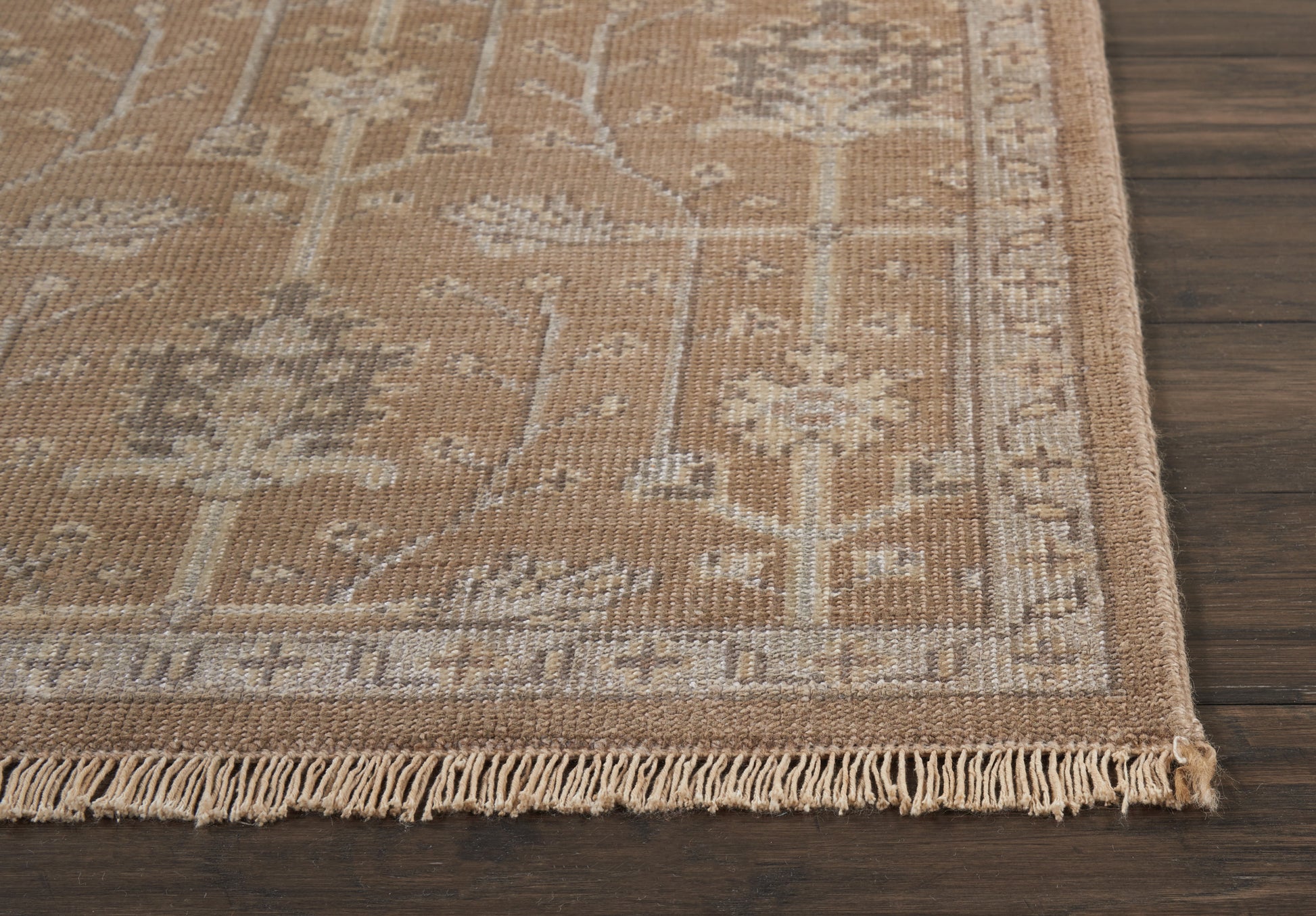 Beige oriental rug with floral border and tassel fringe on dark wood floor.