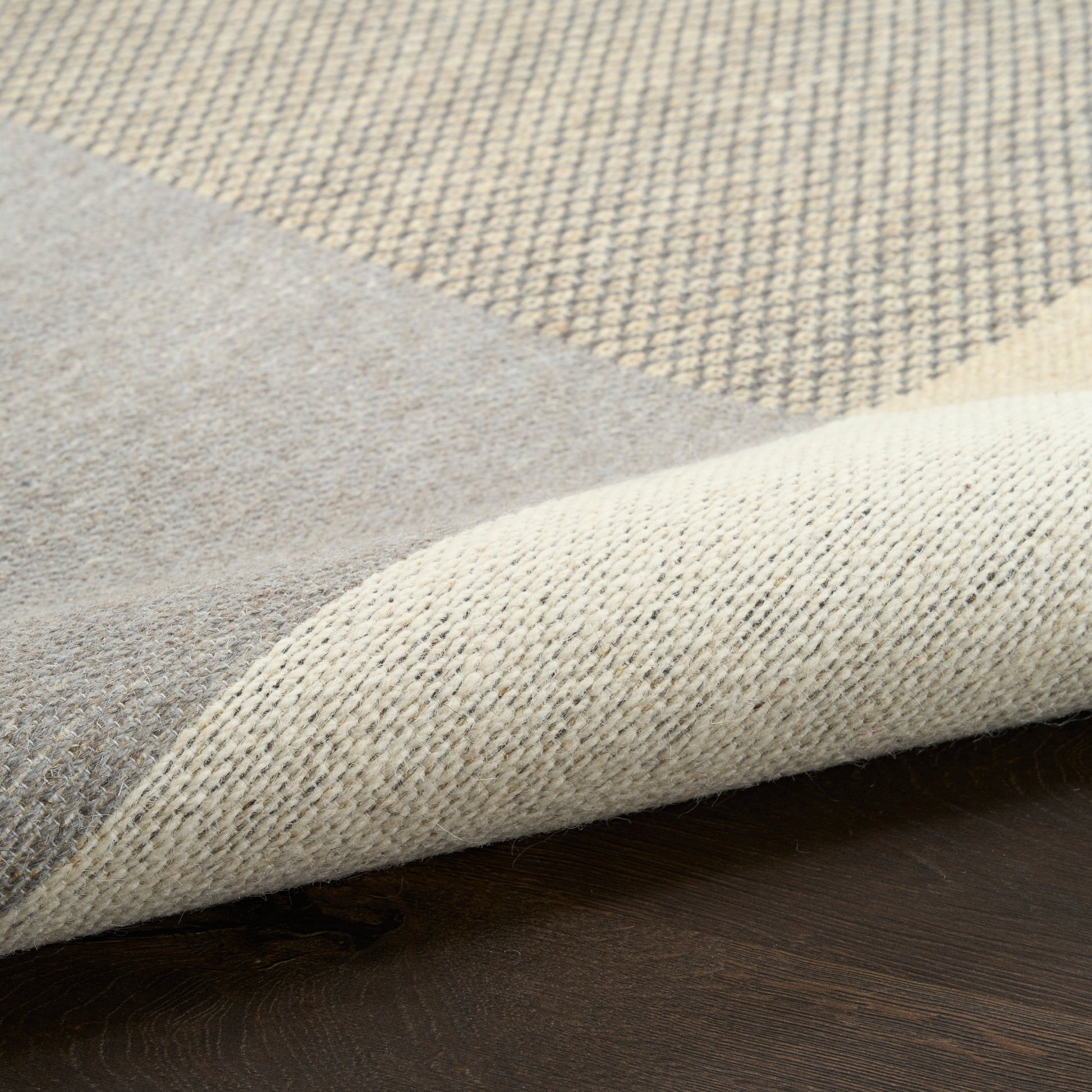 Beige and gray woven rug with color-block design and a folded corner on a dark wooden floor.