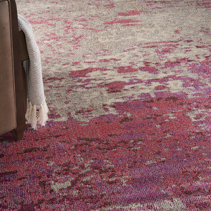 Abstract pink and purple area rug with beige tones, beside a brown leather sofa and cream knit throw.