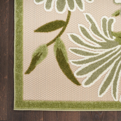 Beige tufted area rug with olive-green border and large leafy botanical motif in green and white on wood floor.