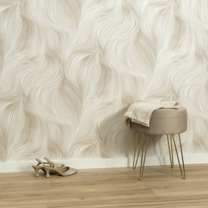 Beige wavy wallpaper backdrop, round upholstered stool with gold legs, cream knit throw, beige sandals on wood floor.
