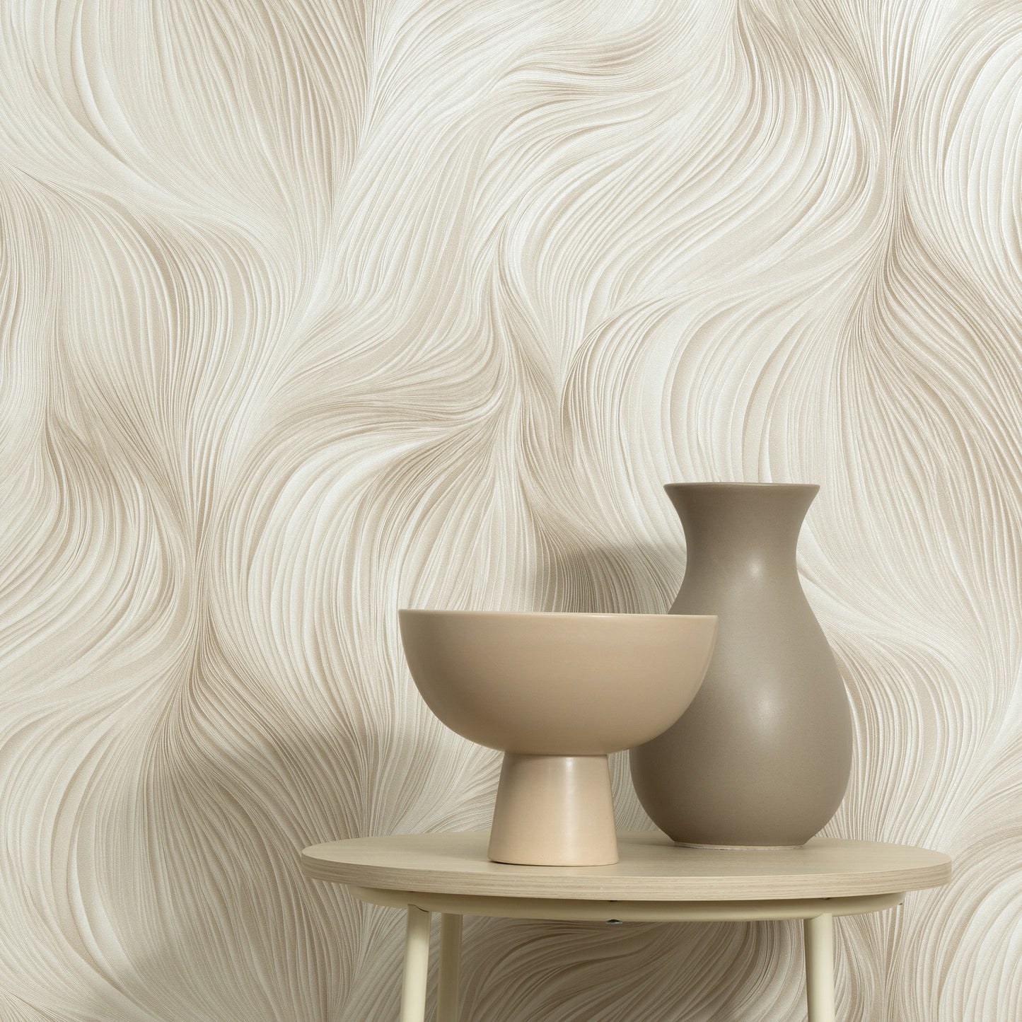 Beige Waves of Light wallpaper pattern as backdrop, with a beige ceramic pedestal bowl and taupe vase on a round light wood table.