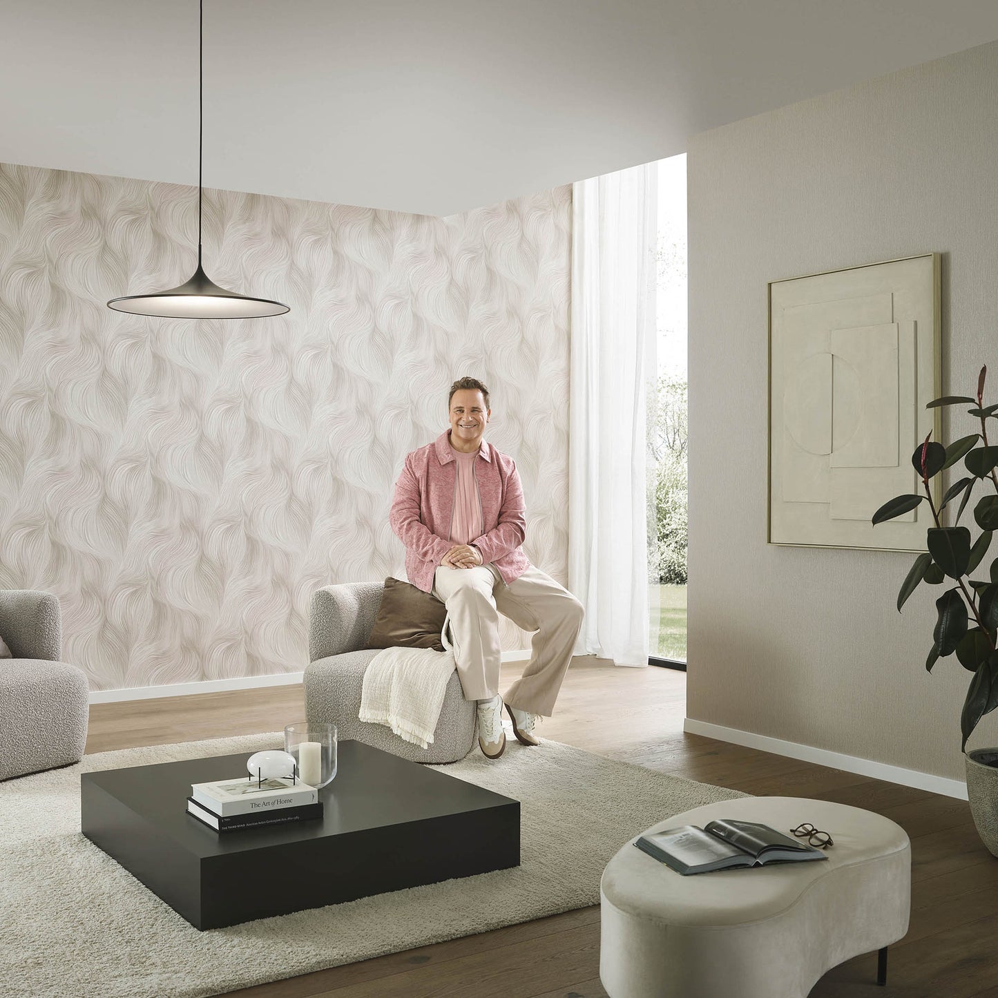 Modern living room with waves of light pink wallpaper, gray seating, black square coffee table, beige rug, plant.