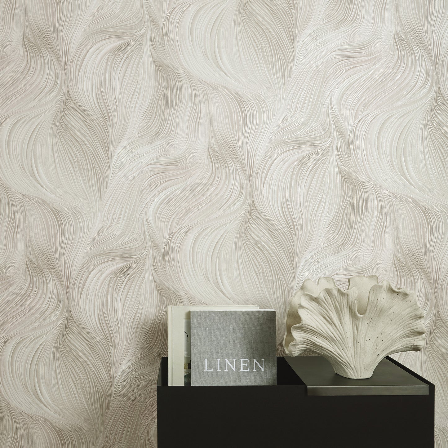 Cream linen-pattern wallpaper with flowing waves; black stand holds a gray 'LINEN' book and a white shell sculpture.