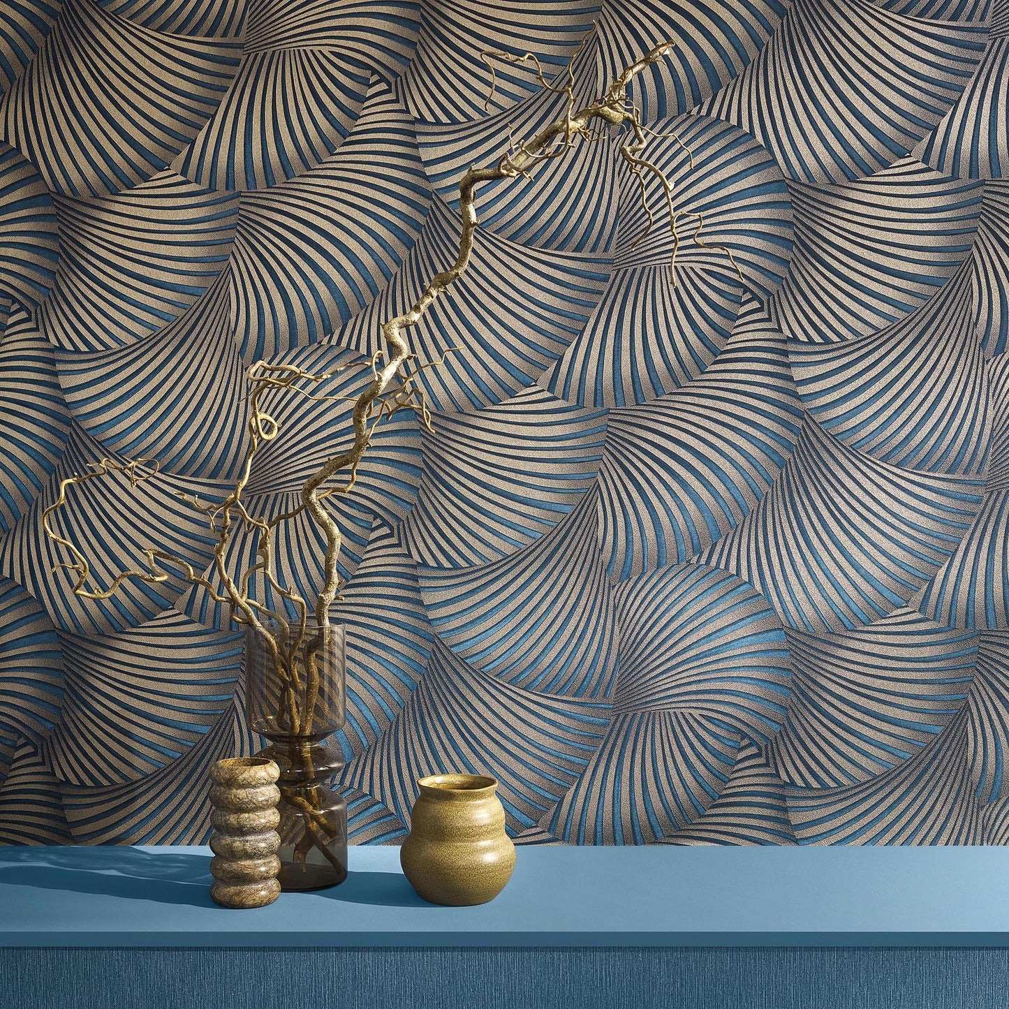 Gold ceramic pot and glass vase with twisted dried branch and beaded stack on blue shelf, against spiral wallpaper.