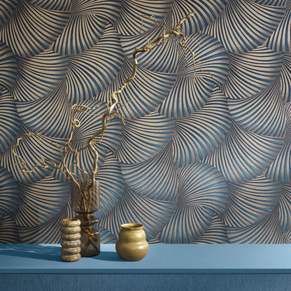 Gold ceramic pot and glass vase with twisted dried branch and beaded stack on blue shelf, against spiral wallpaper.