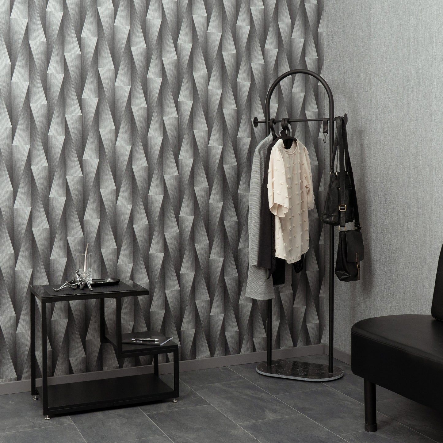 Gray geometric wallpaper with a black metal round-top coat rack, scarves and bags, beside a glass-top console table.