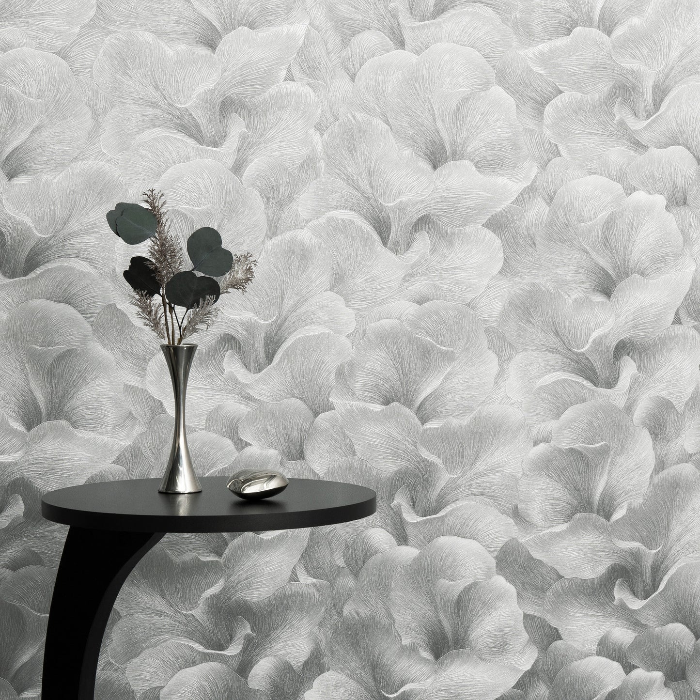 Black round side table with curved leg, silver vase of dried greenery & a metallic dish against grey botanical wallpaper.