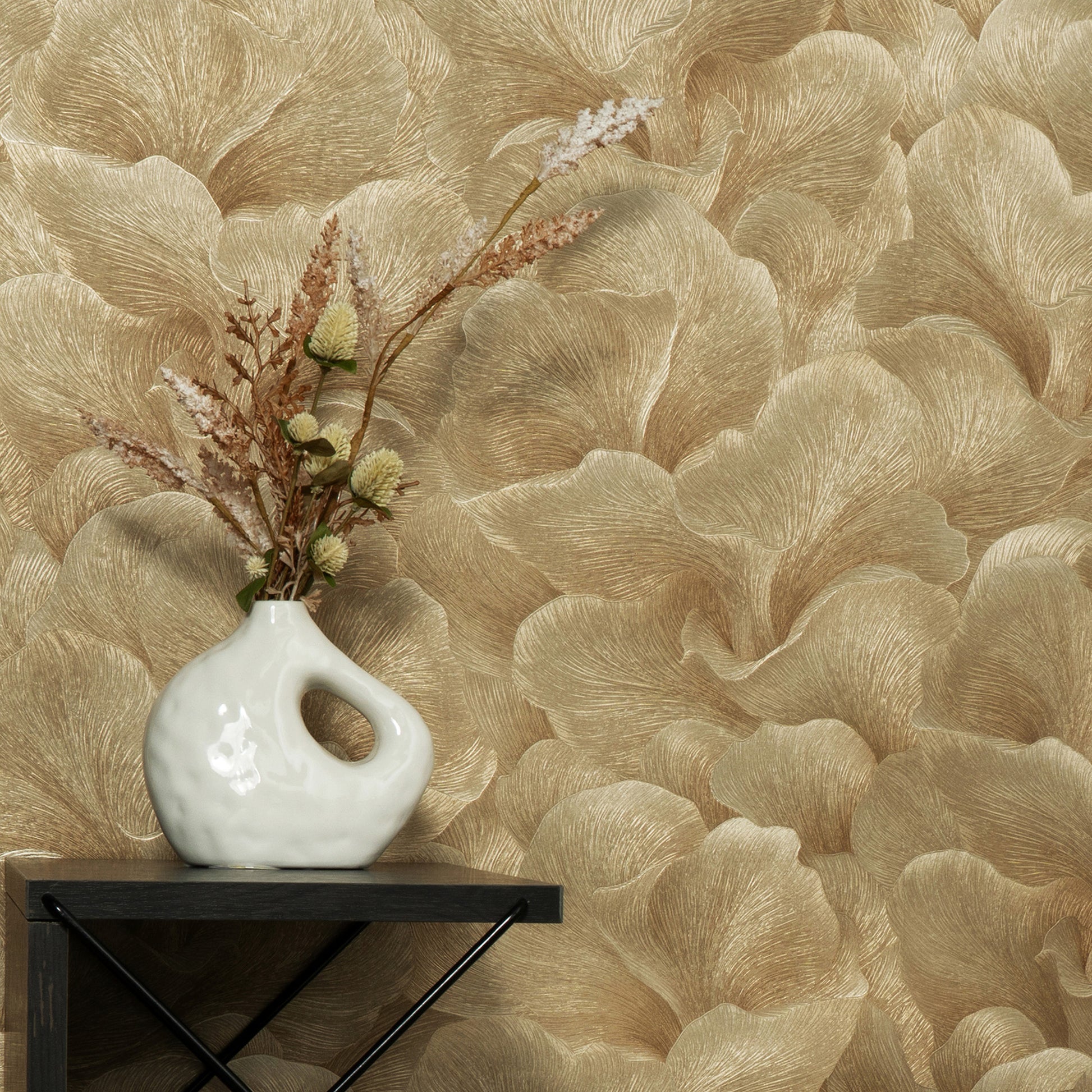 White ceramic vase with a loop handle on a dark shelf, against gold beige palm-leaf wallpaper and dried floral stems.