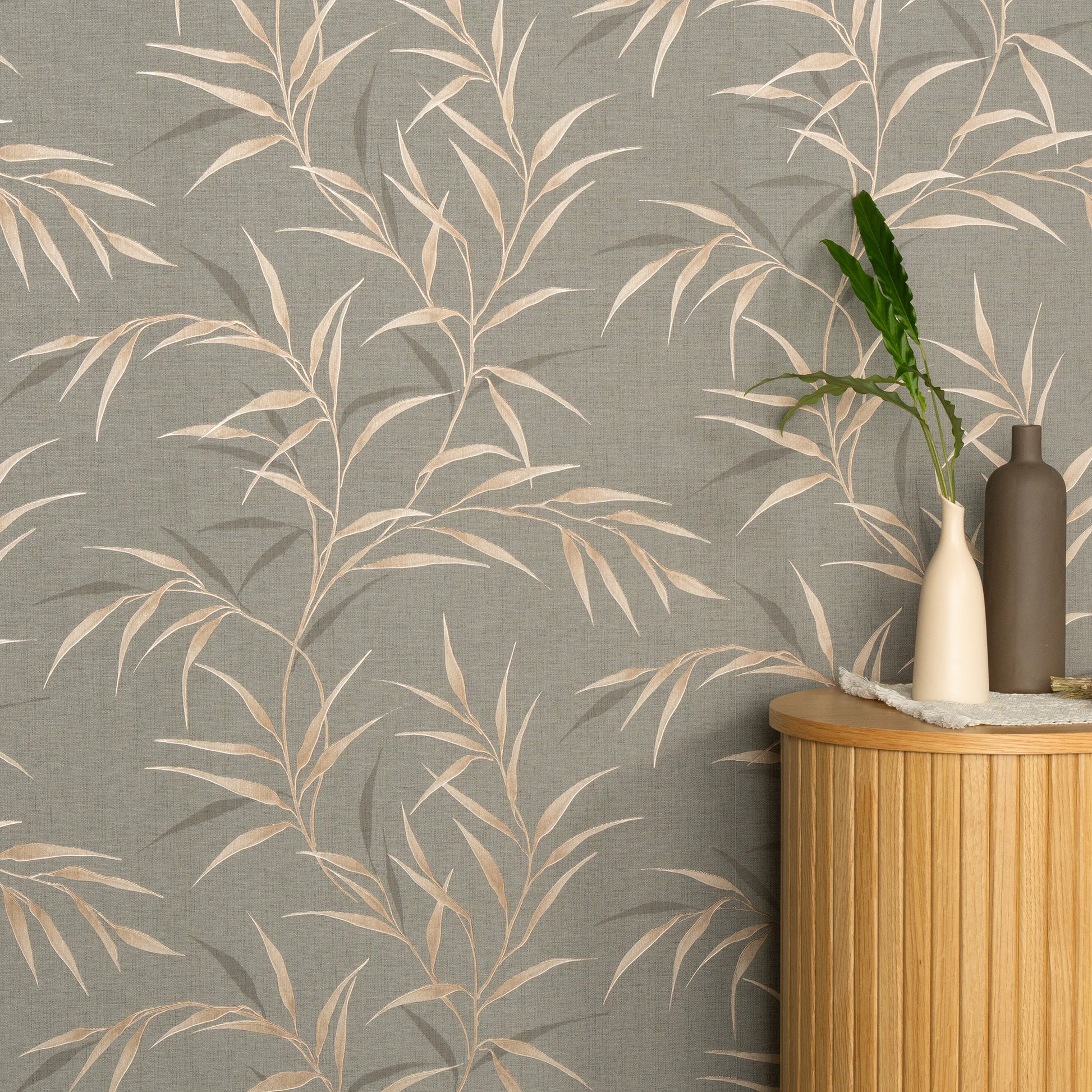 Brown Yamato Leaves wallpaper with nature-inspired leaf pattern; round light-wood cabinet topped with ceramic vases and greenery.