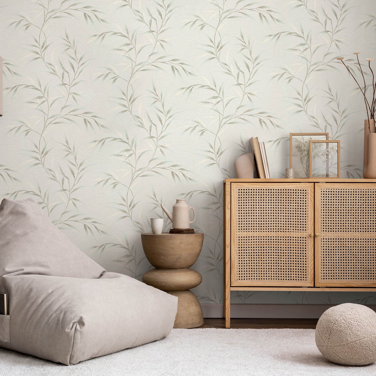 Neutral living room with a woven cane cabinet, beige bean bag, round wood stool, soft rug, and teal Yamato Leaves wallpaper.