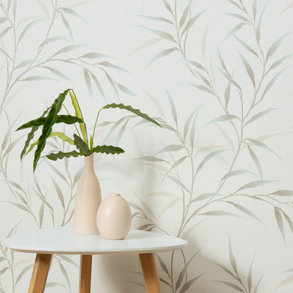 Tall beige vase with a leafy green plant and a small beige egg-shaped vase on a round white table, against pale leafy wallpaper.