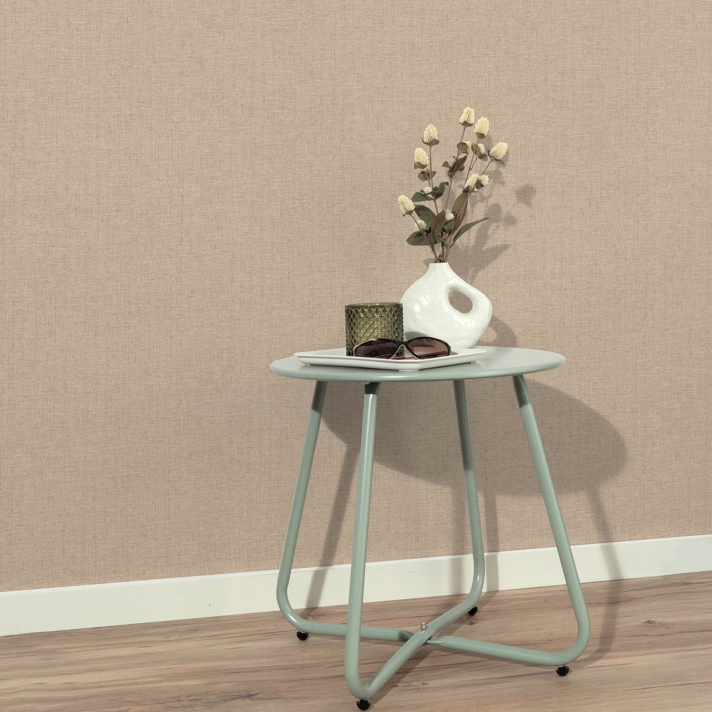 Tan jute-textured wallpaper with an abstract traditional pattern; foreground shows a mint round side table with curved metal legs, a white vase with dried flowers, a dark glass candle holder and sunglasses.