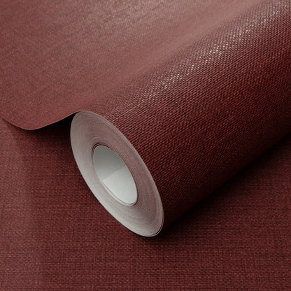 Burgundy textured wallpaper roll with fabric-like weave, partially unrolled, deep red-brown matte finish.
