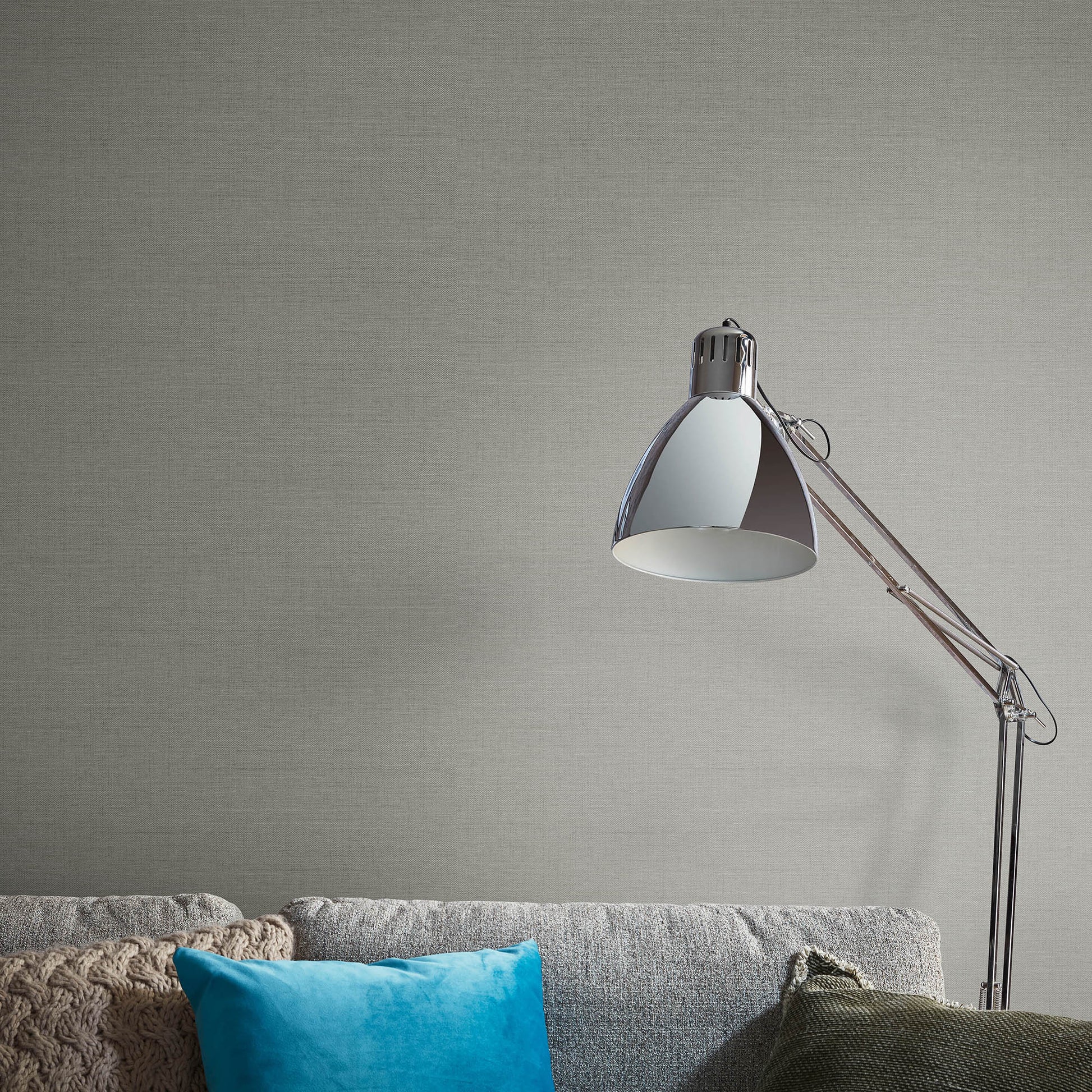Brown jute-texture wallpaper with an abstract traditional pattern on the wall behind a gray sofa with a blue cushion and beige knitted throw.