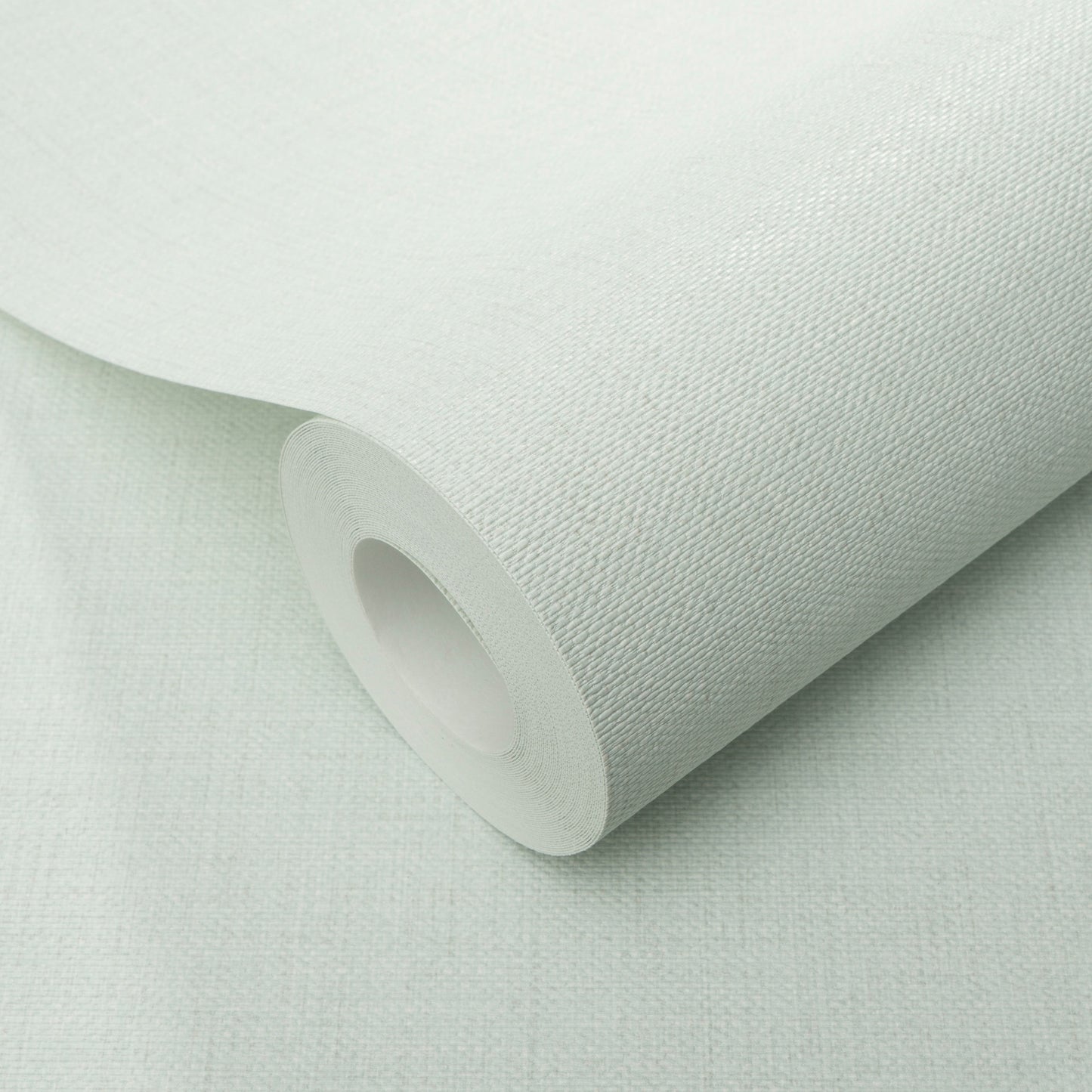 Teal wallpaper roll with visible jute texture, partially unrolled on a pale surface.