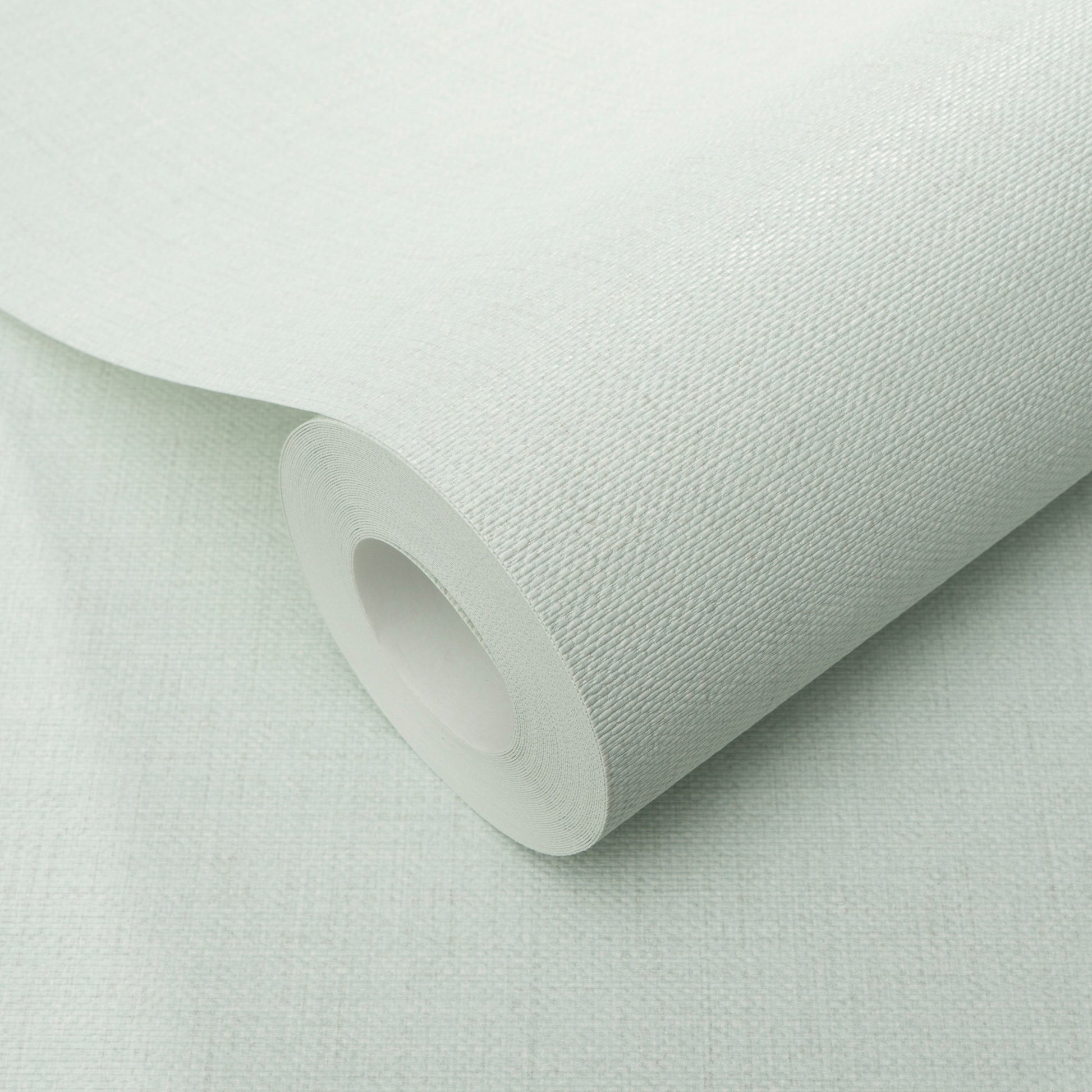 Teal wallpaper roll with visible jute texture, partially unrolled on a pale surface.
