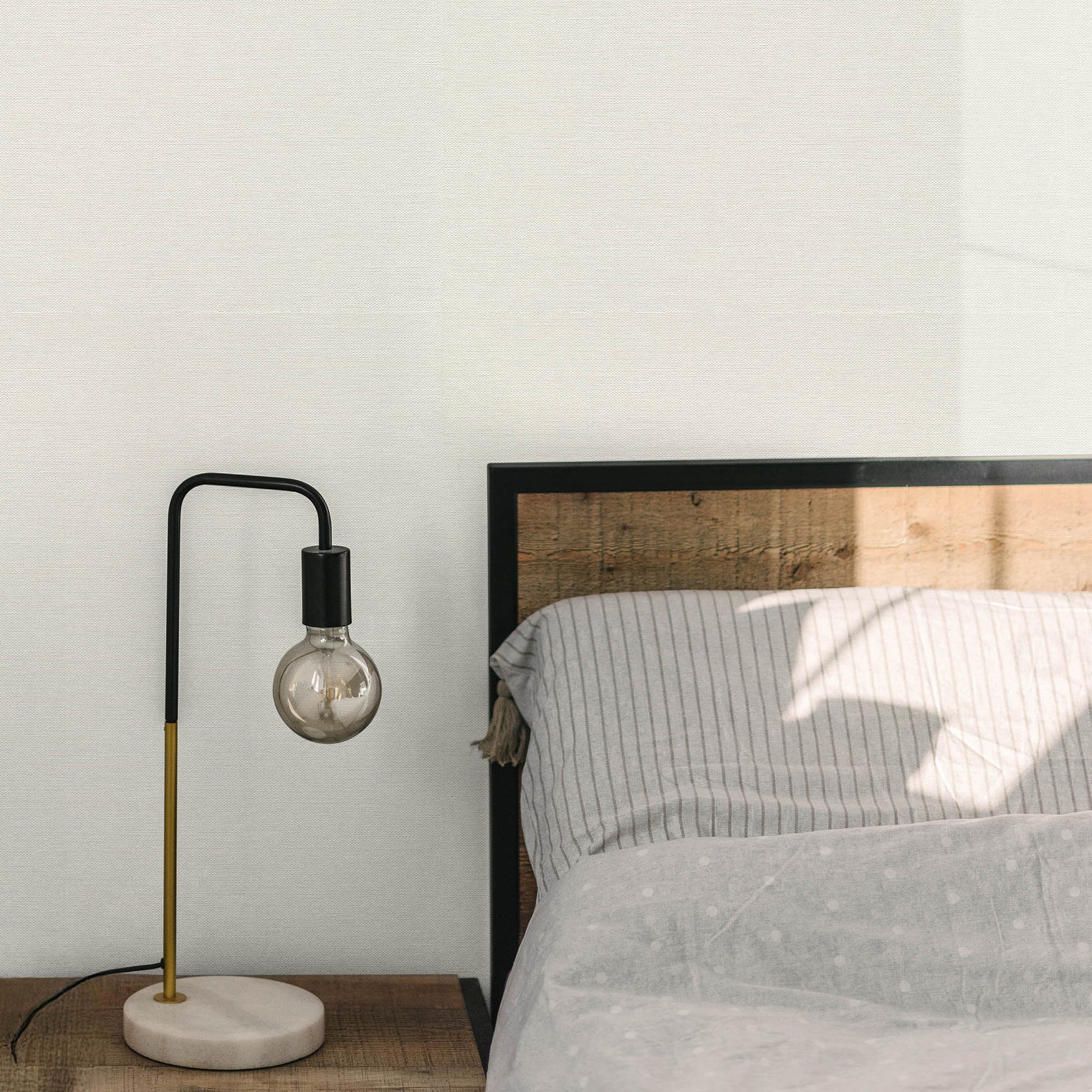 Off-white wallpaper with a jute texture and abstract traditional pattern on the wall behind a bed in a bedroom.