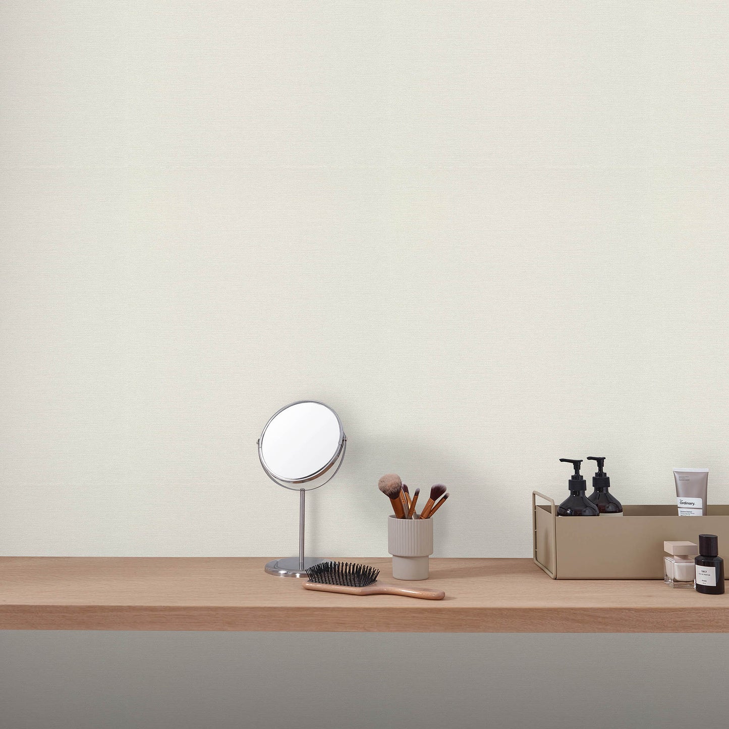 Wood vanity shelf with round silver-framed mirror, makeup brushes in a cup, and black skincare bottles.