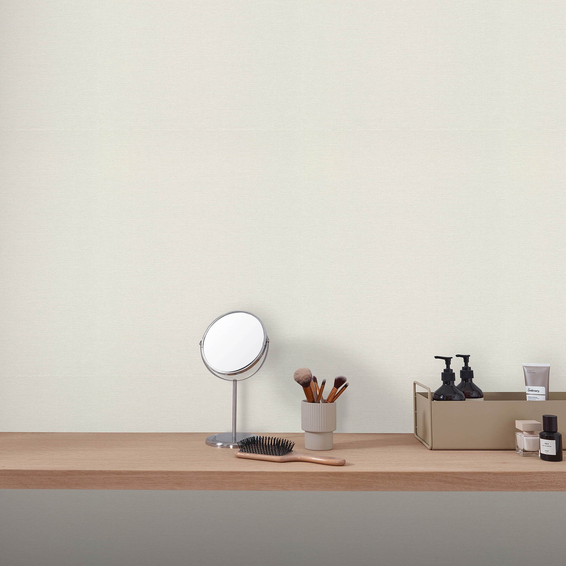 Wood vanity shelf with round silver-framed mirror, makeup brushes in a cup, and black skincare bottles.