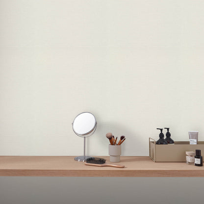 Wood vanity shelf with round silver-framed mirror, makeup brushes in a cup, and black skincare bottles.