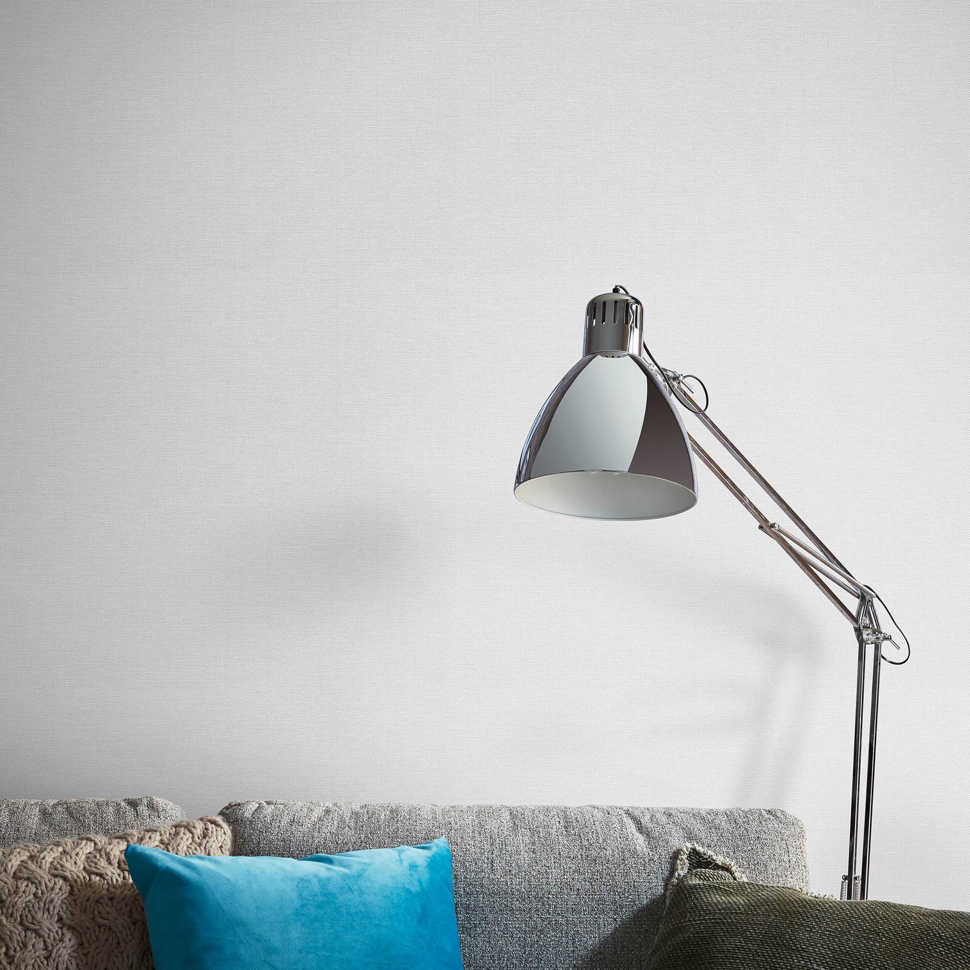 Adjustable metal floor lamp with a dome shade beside a gray fabric sofa and blue throw pillow in a minimalist living room.